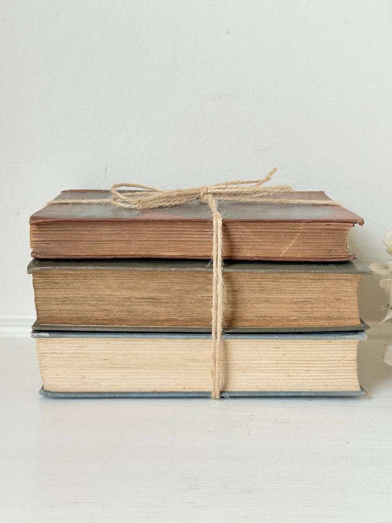 Vintage decorative book bundle in red, olive green and cream tied with twine, photographed on a white surface