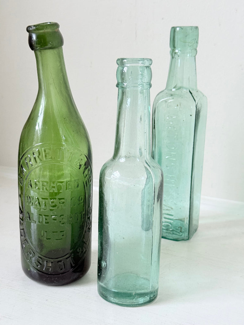 Trio of antique aqua and green glass bottles with embossed lettering, photographed on a white surface