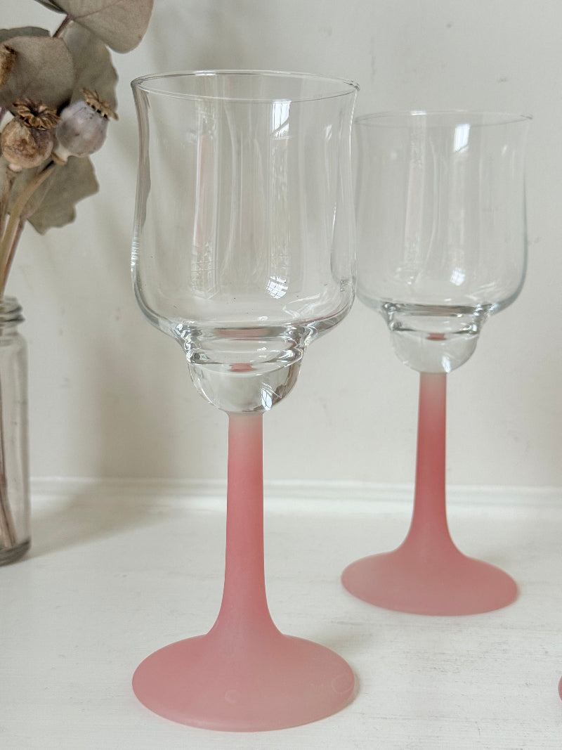 Set of five vintage wine glasses with clear bowls and pink stems photographed on a white surface.