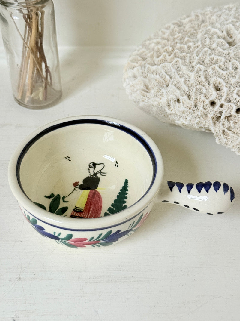 French Quimper faience handled olive bowl with Petit Breton figure and blue rim, photographed on a white surface