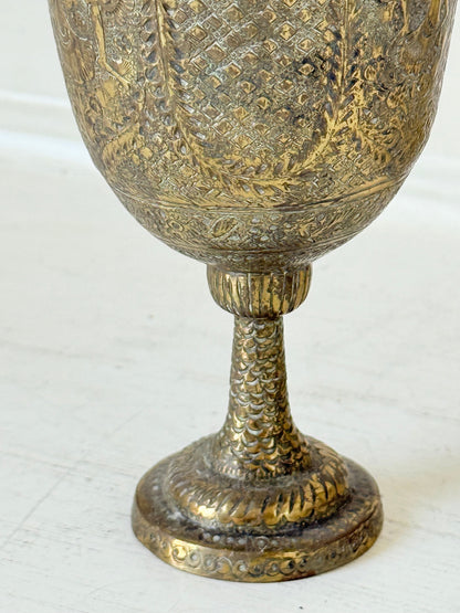 Indian Benares brass chalice vase with figural panels and pedestal base, photographed on a white surface