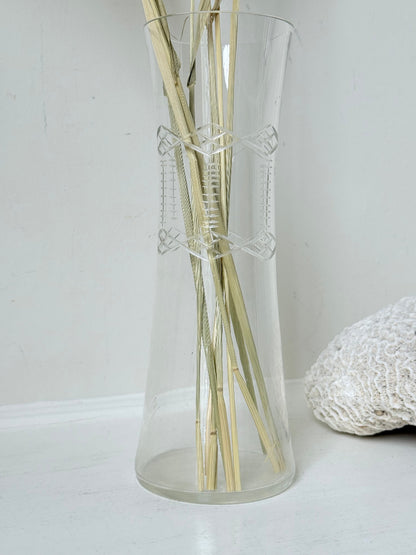 Vintage clear glass cylinder vase with etched leaf design, photographed on a white surface.