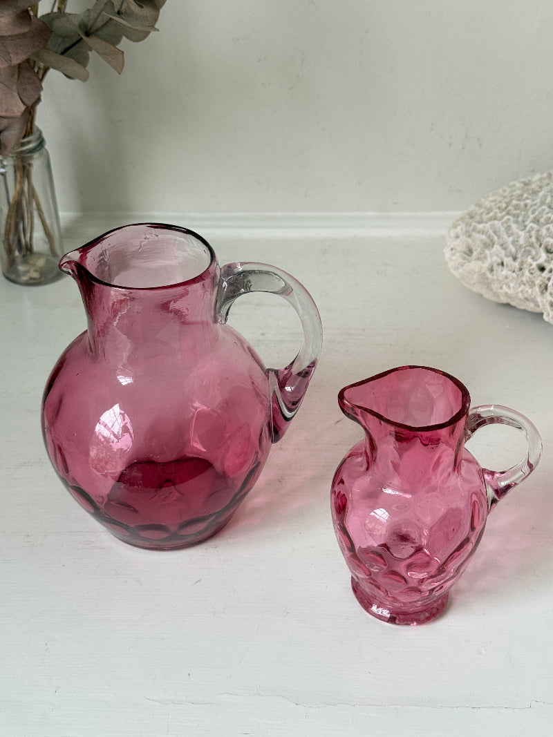 Vintage cranberry glass jugs, a pair with clear handles, photographed on a white surface