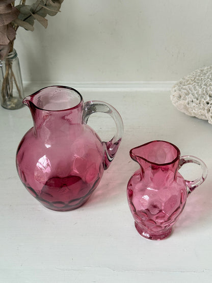 Vintage cranberry glass jugs, a pair with clear handles, photographed on a white surface