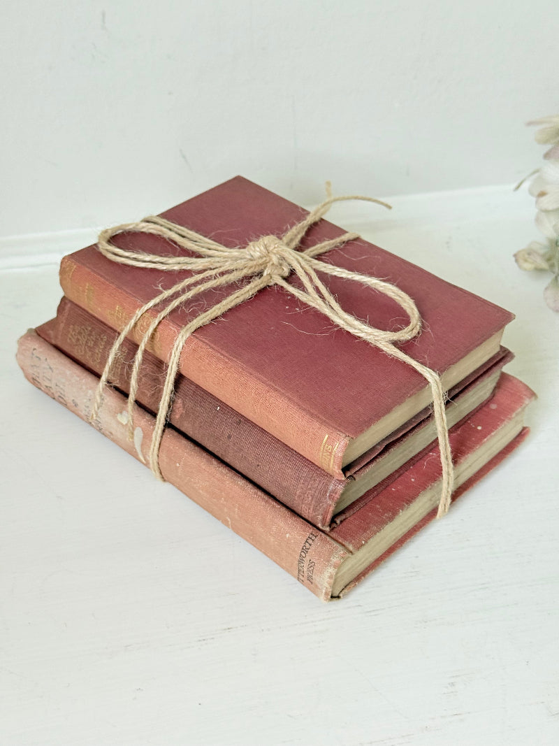 Bundle of three vintage books in worn rose and blush tones tied with natural twine, photographed on a white surface
