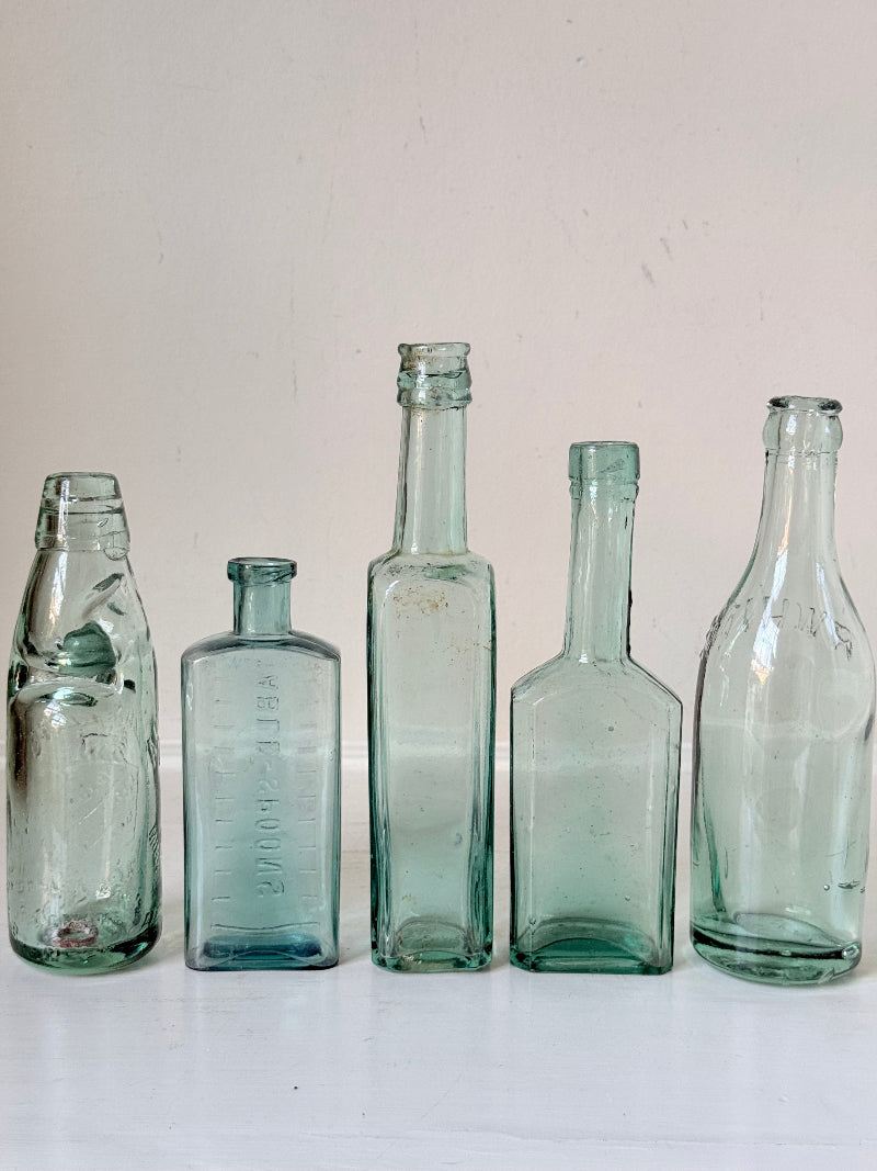 Set of five antique aqua green glass bottles with embossed lettering, photographed on a white surface
