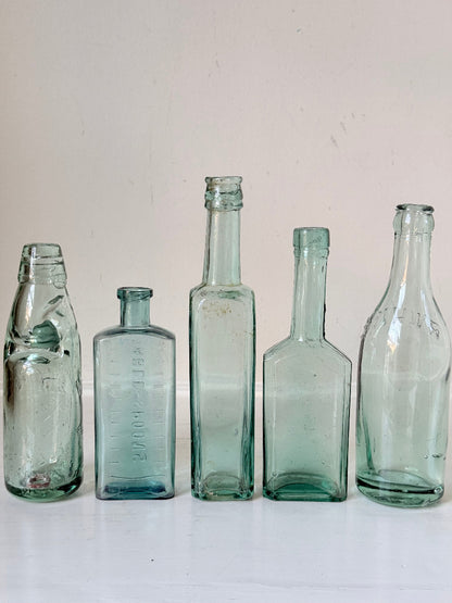Set of five antique aqua green glass bottles with embossed lettering, photographed on a white surface