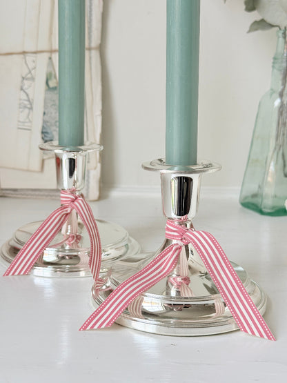 Pair of silver tone candlesticks with wide round stepped bases holding green candles, photographed on a white surface
