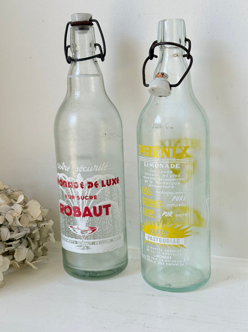 Pair of vintage French glass bottles with retro typography and graphics, photographed on a white surface