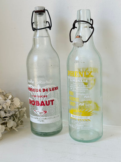 Pair of vintage French glass bottles with retro typography and graphics, photographed on a white surface