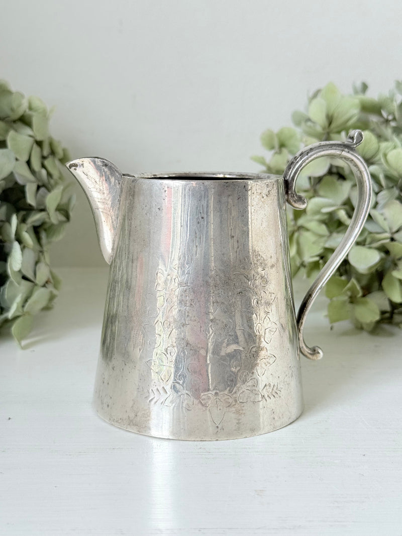 vintage silver plate jug with curved handle photographed on white surface with green hydrangeas