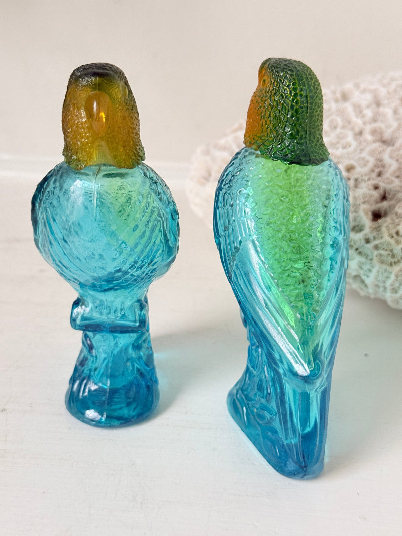 Pair of vintage Avon turquoise glass parrot bottles with green amber stoppers photographed on a white surface