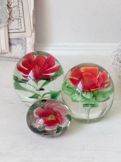 Trio of vintage glass paperweights with hand worked red floral detail, clear glass domes and green leaf decoration