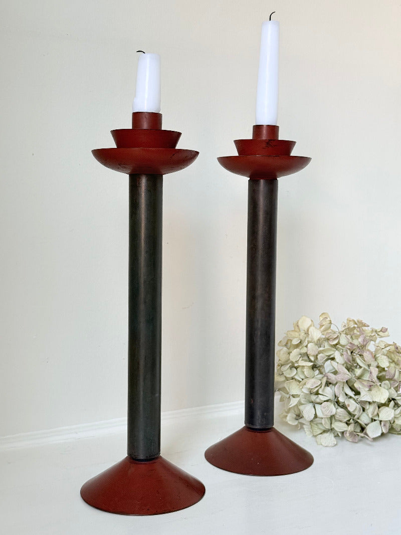 Pair of tall vintage metal candlesticks in black and burgundy, styled with white taper candles on a white surface.