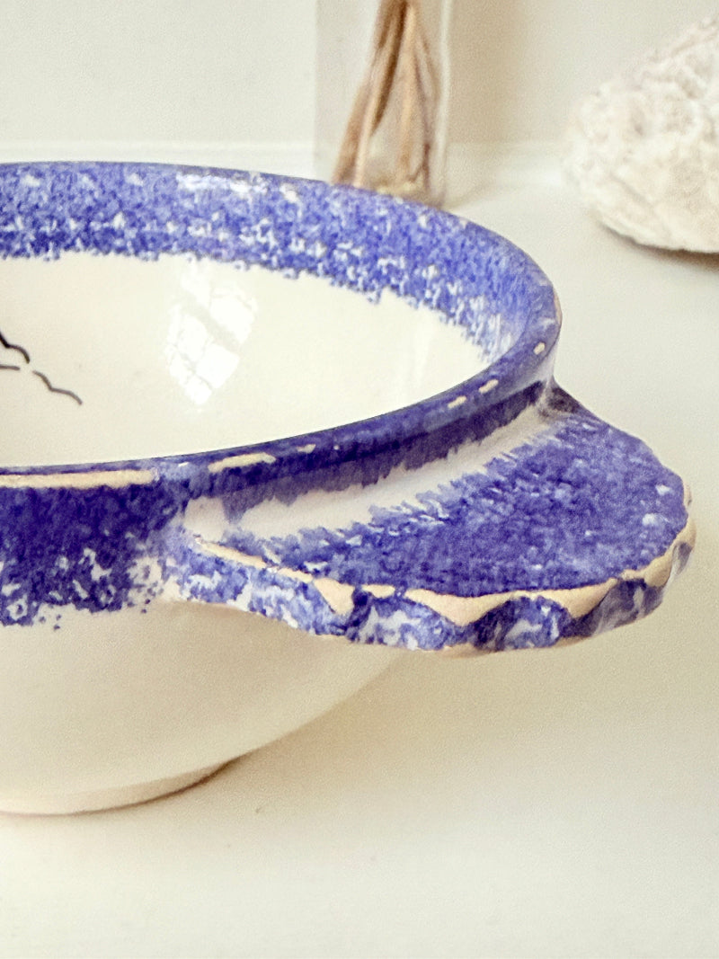 Quimper faience olive bowl with Petit Breton figure and blue speckled rim photographed on a white surface