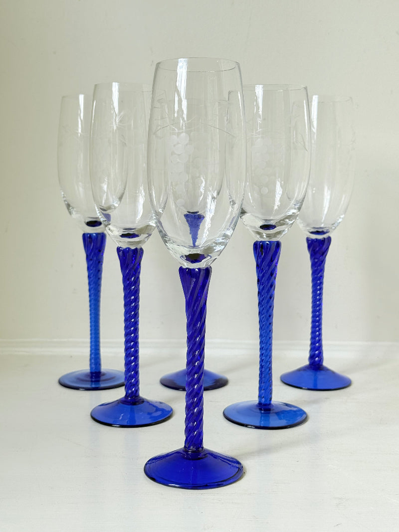 Set of six vintage French champagne flutes with tall clear bowls and cobalt blue twisted stems, photographed on white surface.