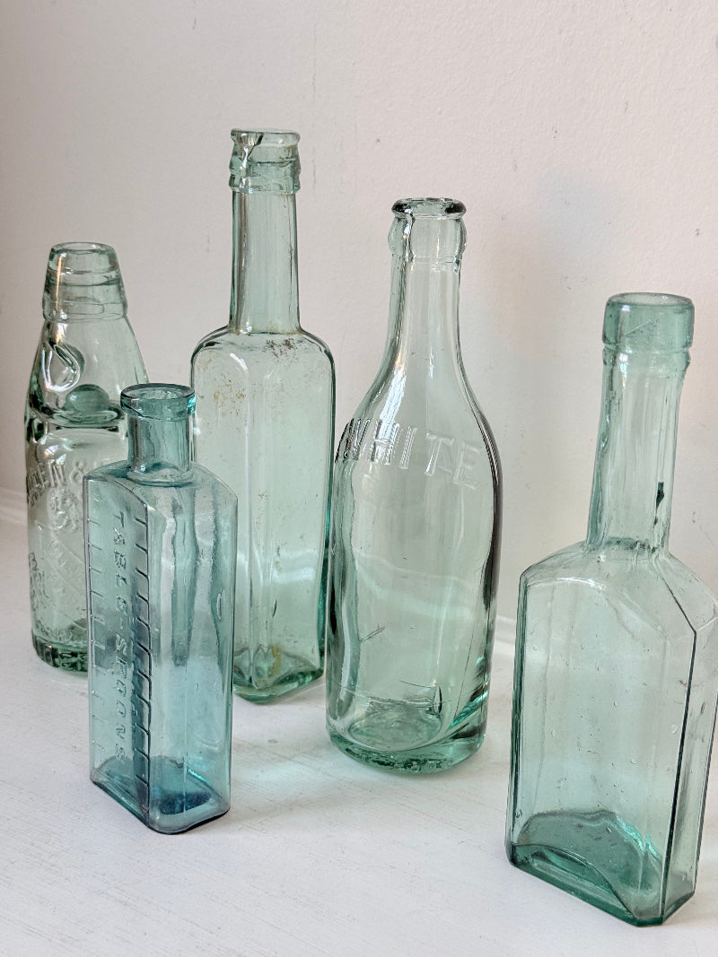 Set of five antique aqua green glass bottles with embossed lettering, photographed on a white surface