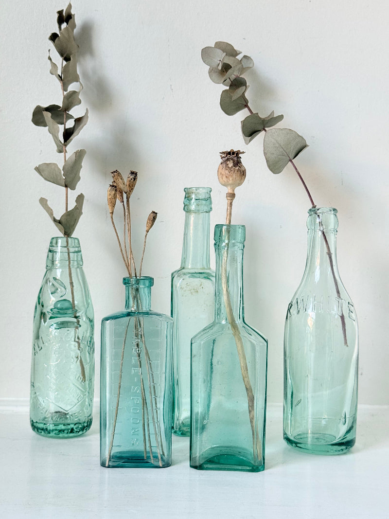 Set of five antique aqua green glass bottles with embossed lettering, photographed on a white surface