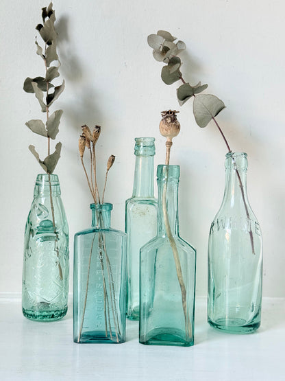 Set of five antique aqua green glass bottles with embossed lettering, photographed on a white surface