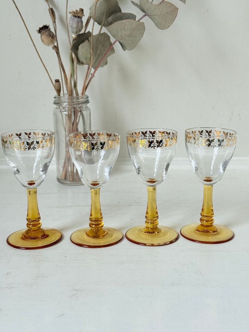 Vintage set of four shot glasses with amber stems and gilt rims, photographed on a white surface