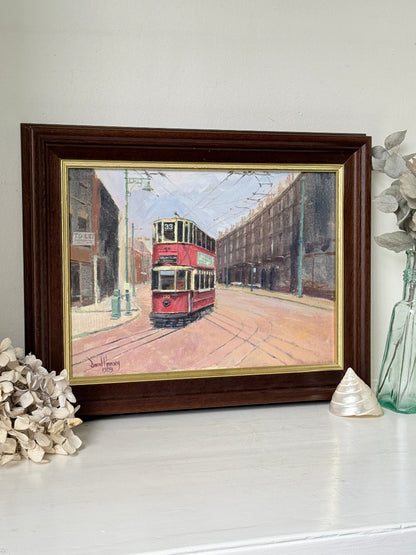 A framed vintage oil painting of a red double-decker tram on a city street, displayed on a white shelf with decorative dried flowers and a glass vase.