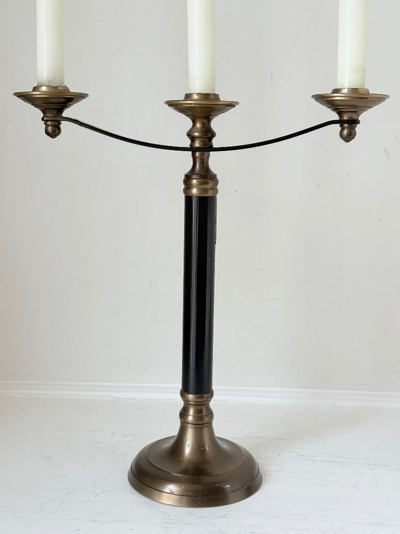 Vintage three arm candelabra in brass and ebonised metal with ivory taper candles styled on a white surface