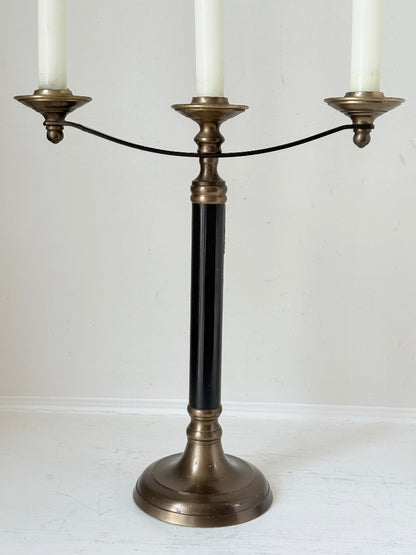 Vintage three arm candelabra in brass and ebonised metal with ivory taper candles styled on a white surface
