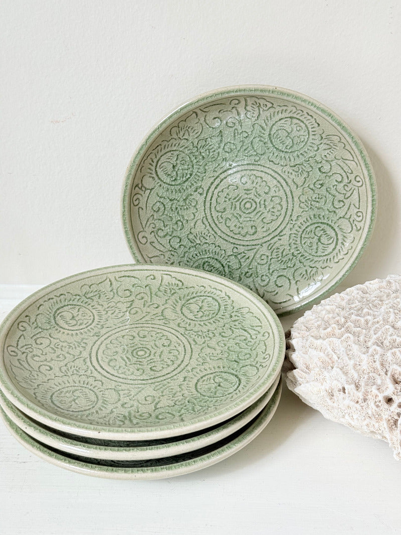 Set of four Thai celadon side plates with embossed patterns and sage green crackled glaze, stacked and photographed on white surface