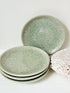 Set of four Thai celadon side plates with embossed patterns and sage green crackled glaze, stacked and photographed on white surface