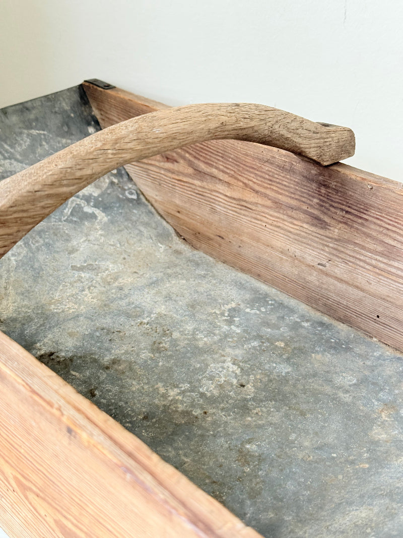Vintage zinc and wood garden trug with arched wooden handle photographed on a white surface