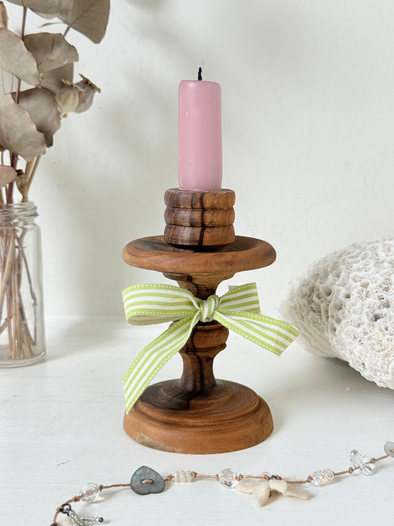 Vintage olivewood candlestick photographed on a white surface, turned wooden stem with warm grain and wide base holding a pink taper candle
