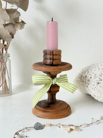 Vintage olivewood candlestick photographed on a white surface, turned wooden stem with warm grain and wide base holding a pink taper candle