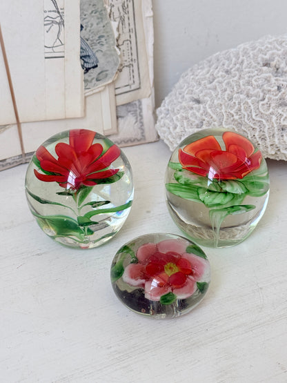 Trio of vintage glass paperweights with hand worked red floral detail, clear glass domes and green leaf decoration