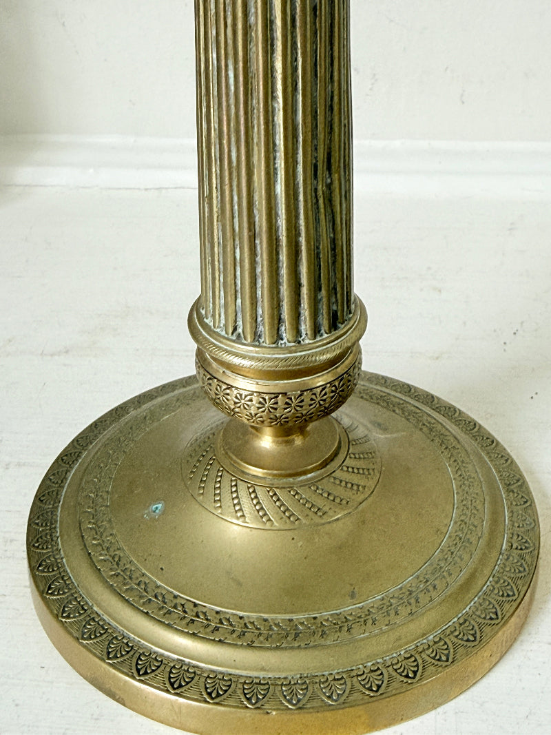 Pair of antique brass Empire style candlesticks photographed on a white surface with fluted columns and circular bases holding pink taper candles