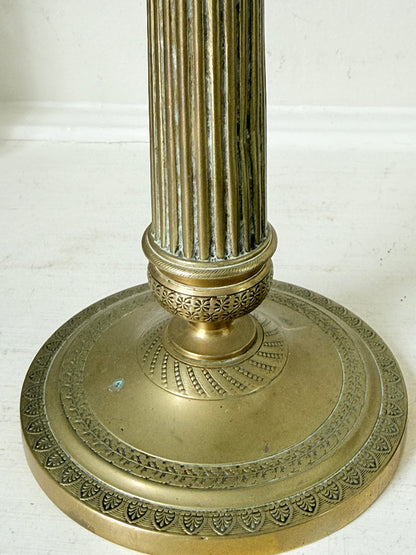 Pair of antique brass Empire style candlesticks photographed on a white surface with fluted columns and circular bases holding pink taper candles