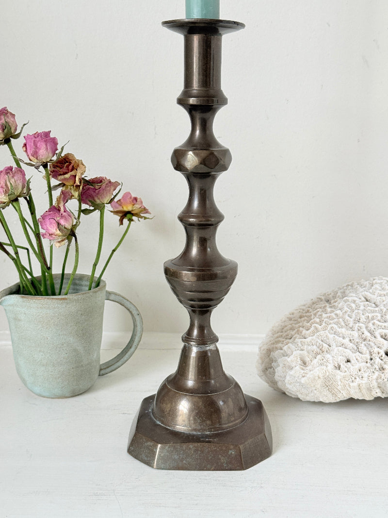 Bronze coloured vintage candlestick with bobbin stem and shaped base styled with taper candle on white surface