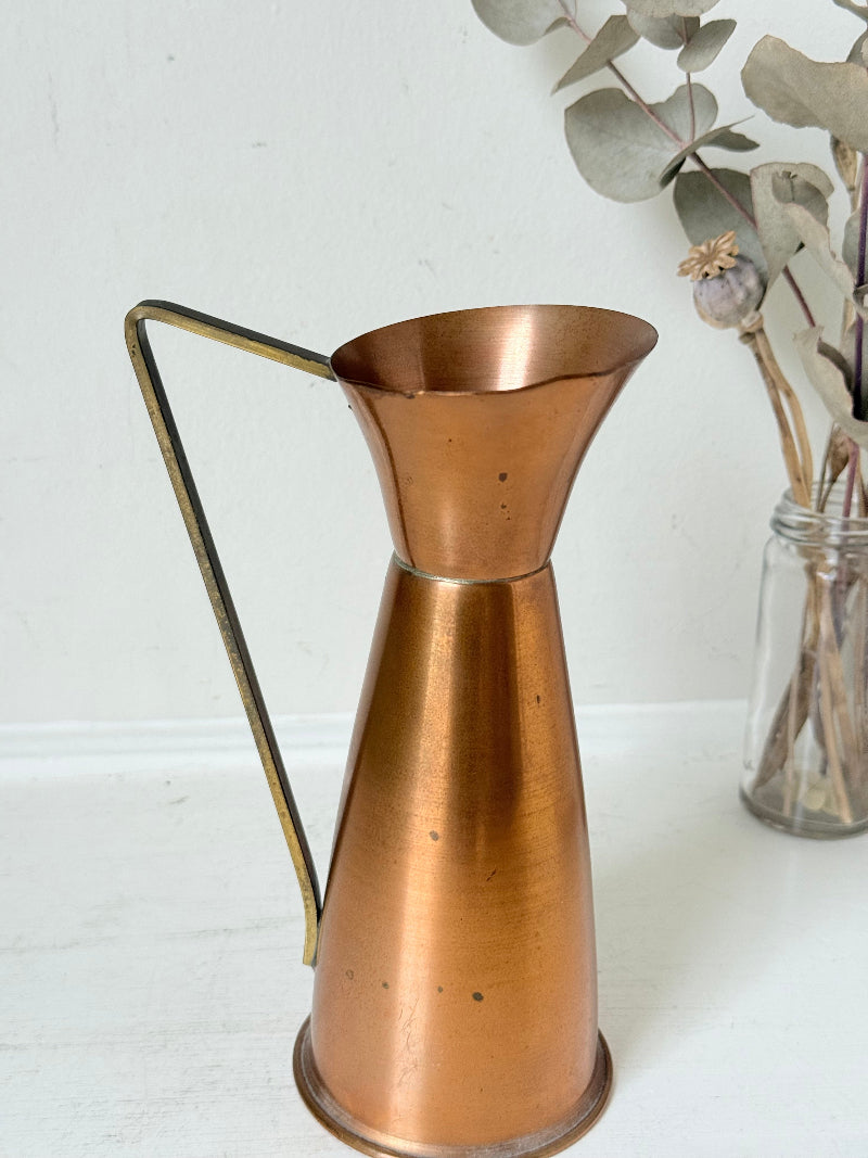 Vintage copper and brass jug with slender handle, photographed on a white surface