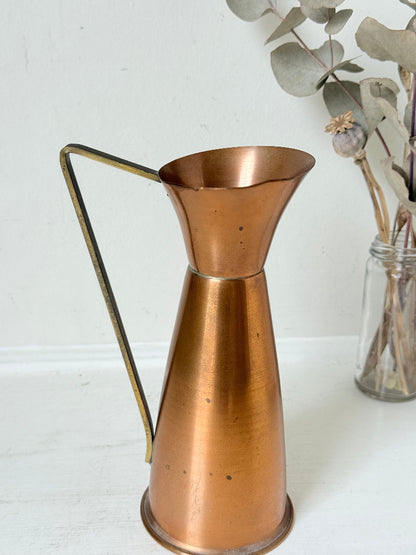 Vintage copper and brass jug with slender handle, photographed on a white surface
