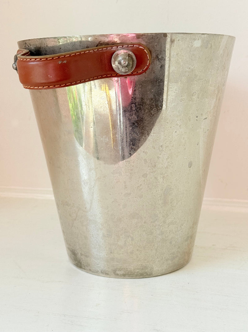 Vintage metal wine cooler with leather handles and tapered form, photographed on white surface.