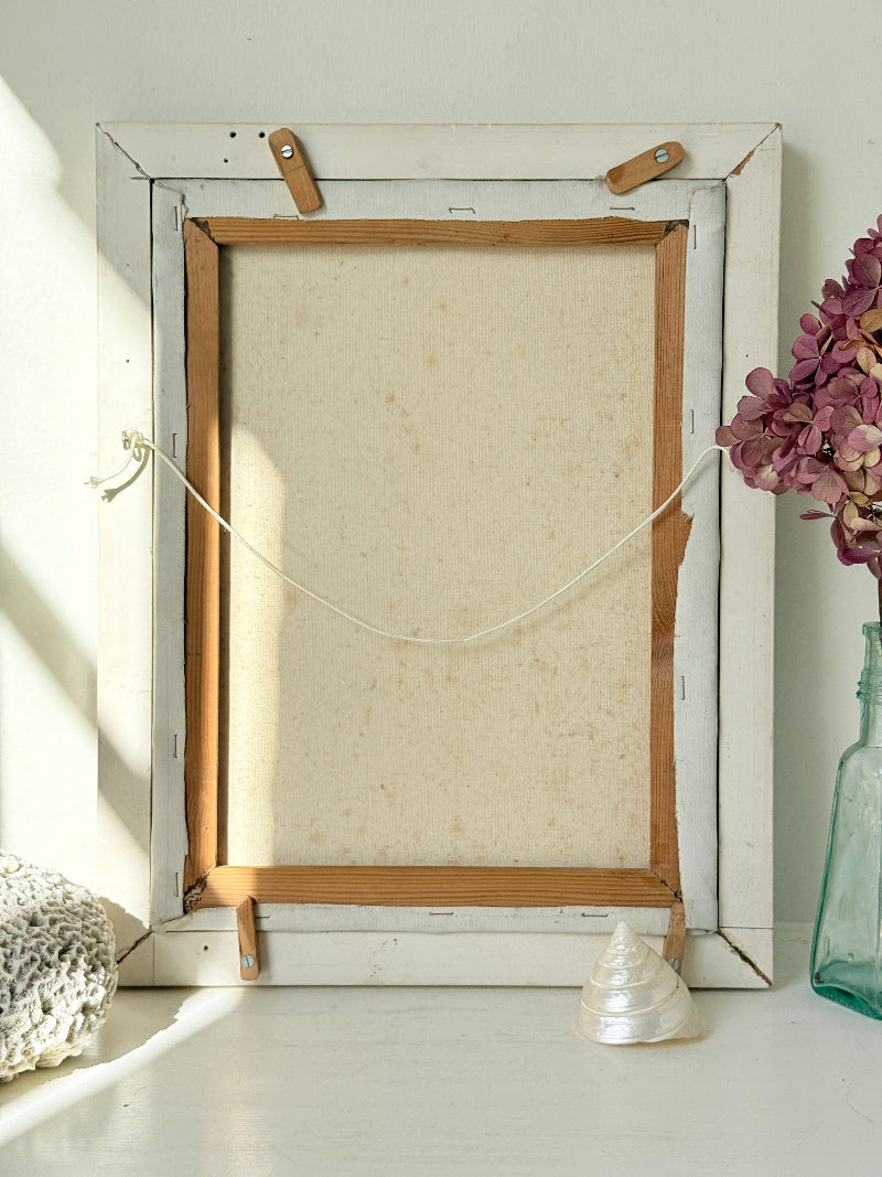 A vintage-style white wooden picture frame with a light beige canvas backing, held together by wooden clips and a string, displayed on a white surface with decorative props.