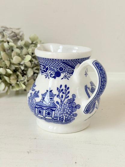 Vintage Churchill Blue Willow milk jug in blue and white ceramic photographed on a white surface.