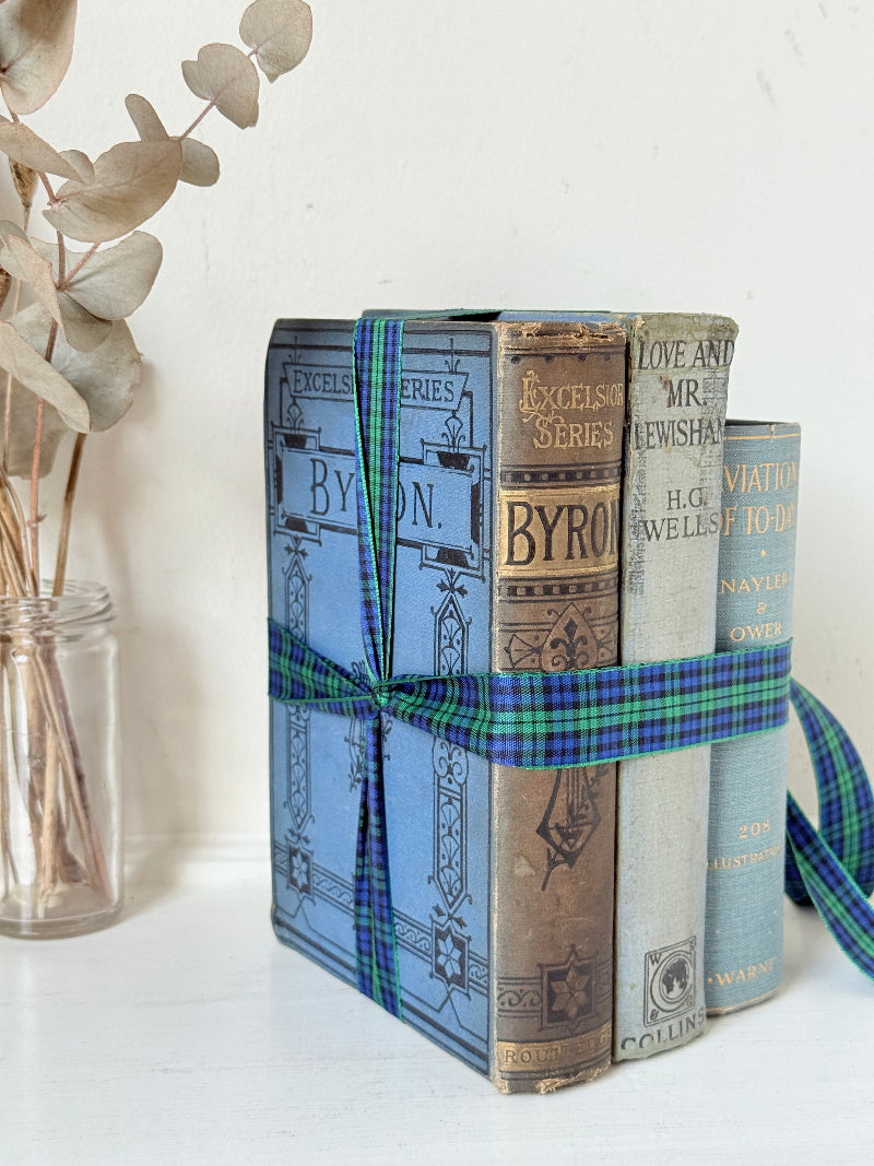 Vintage blue fabric bound decorative book bundle tied with blue and green tartan ribbon, photographed on a white surface