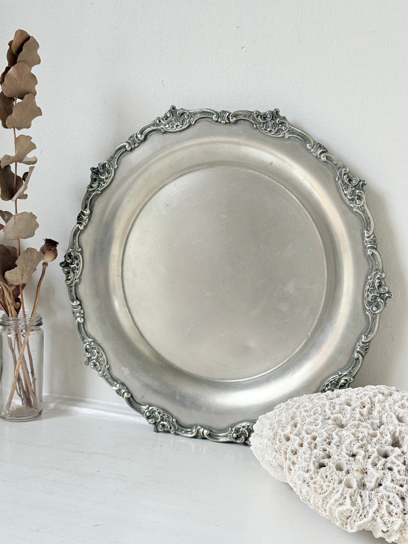 Vintage silvertone metal tray with ornate border, photographed on a white surface