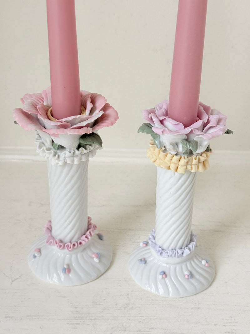 Pair of vintage floral ceramic candlesticks with rose candle cups and pink taper candles styled on a white surface