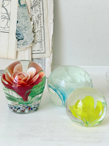 Trio of vintage glass paperweights with red flower, yellow flower and turquoise swirl decoration in clear coloured glass