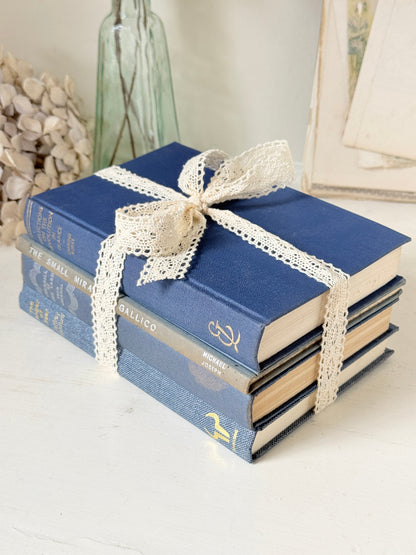 Bundle of vintage blue cloth books with gilt spines tied with ivory lace ribbon for shelf and table styling