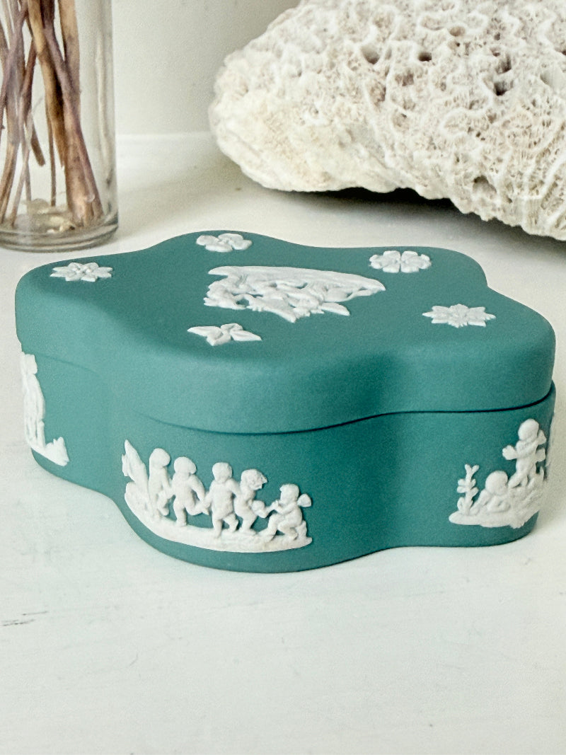 Vintage Wedgwood Jasperware teal green lidded trinket box in a quatrefoil shape, decorated with white neoclassical figures and florets, styled with dried stems.