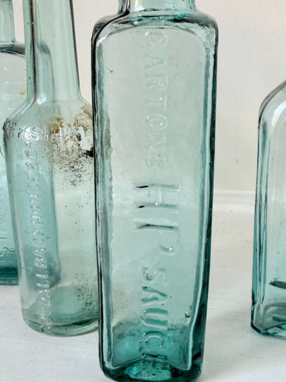 Set of five antique aqua glass bottles with embossed lettering, photographed on a white surface with dried stems
