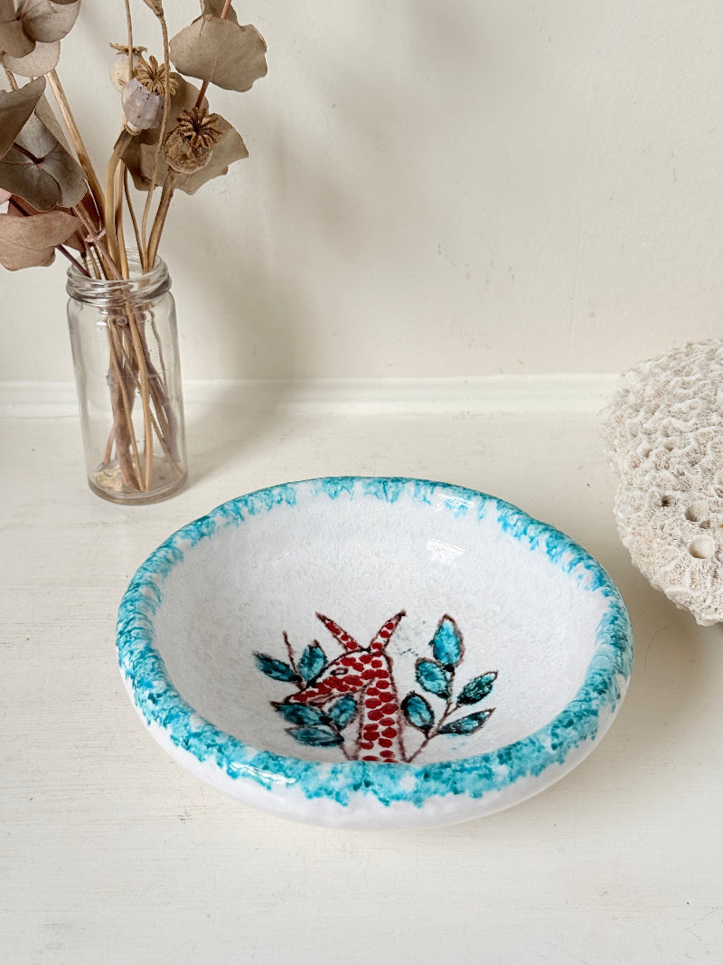 Vintage studio pottery bowl with turquoise rim and red hand painted giraffe motif, photographed on a white surface