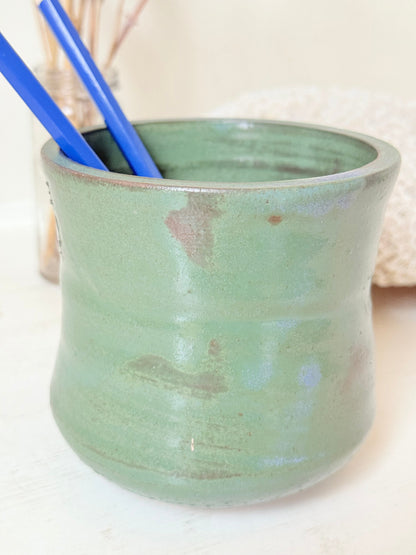 Studio pottery pencil pot in green glaze, handmade on the wheel, photographed on a white surface with pencils inside.